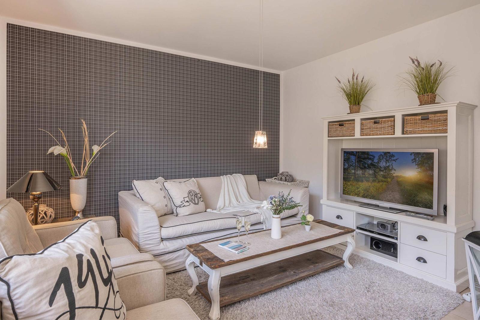 Wohnzimmer mit Sofa, Couchtisch und Fernseher auf weißen Schränken. Wand mit Mosaikfliesen.