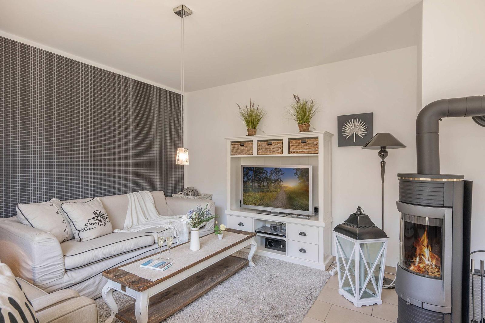 Wohnzimmer mit Sofa, Fernseher und Kaminofen. Wand mit Muster, Holztisch und Lampe.