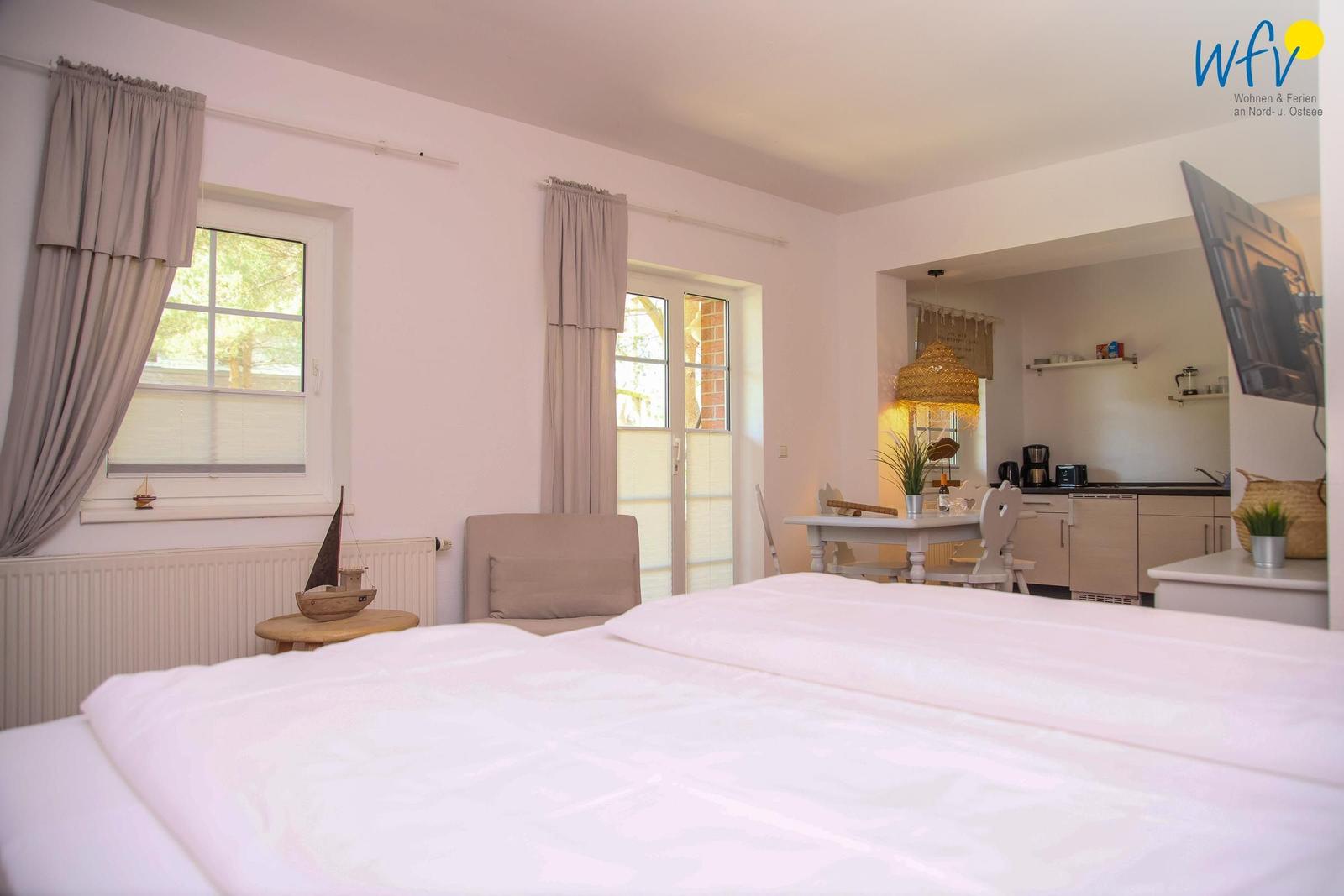 Schlafzimmer mit Blick auf Küche und Essbereich. Fenster und Tür führen nach draußen.