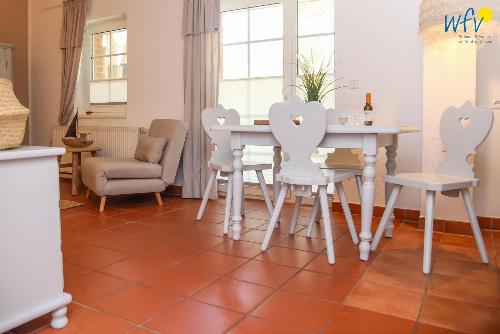 Esszimmer mit weißem Tisch und Stühlen, Terrakottaboden und Fenstern mit Vorhängen.