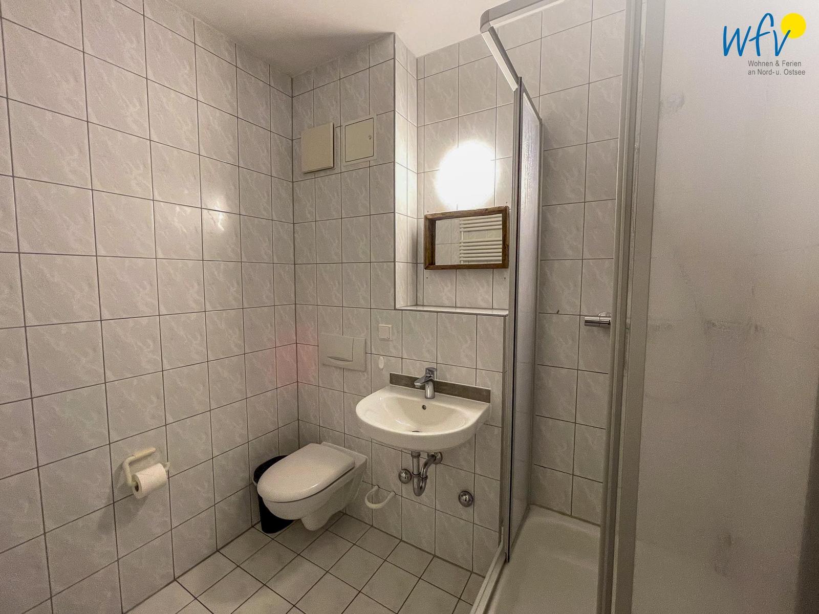 Badezimmer mit Dusche, Waschbecken und WC. Fliesenwand und Spiegel.