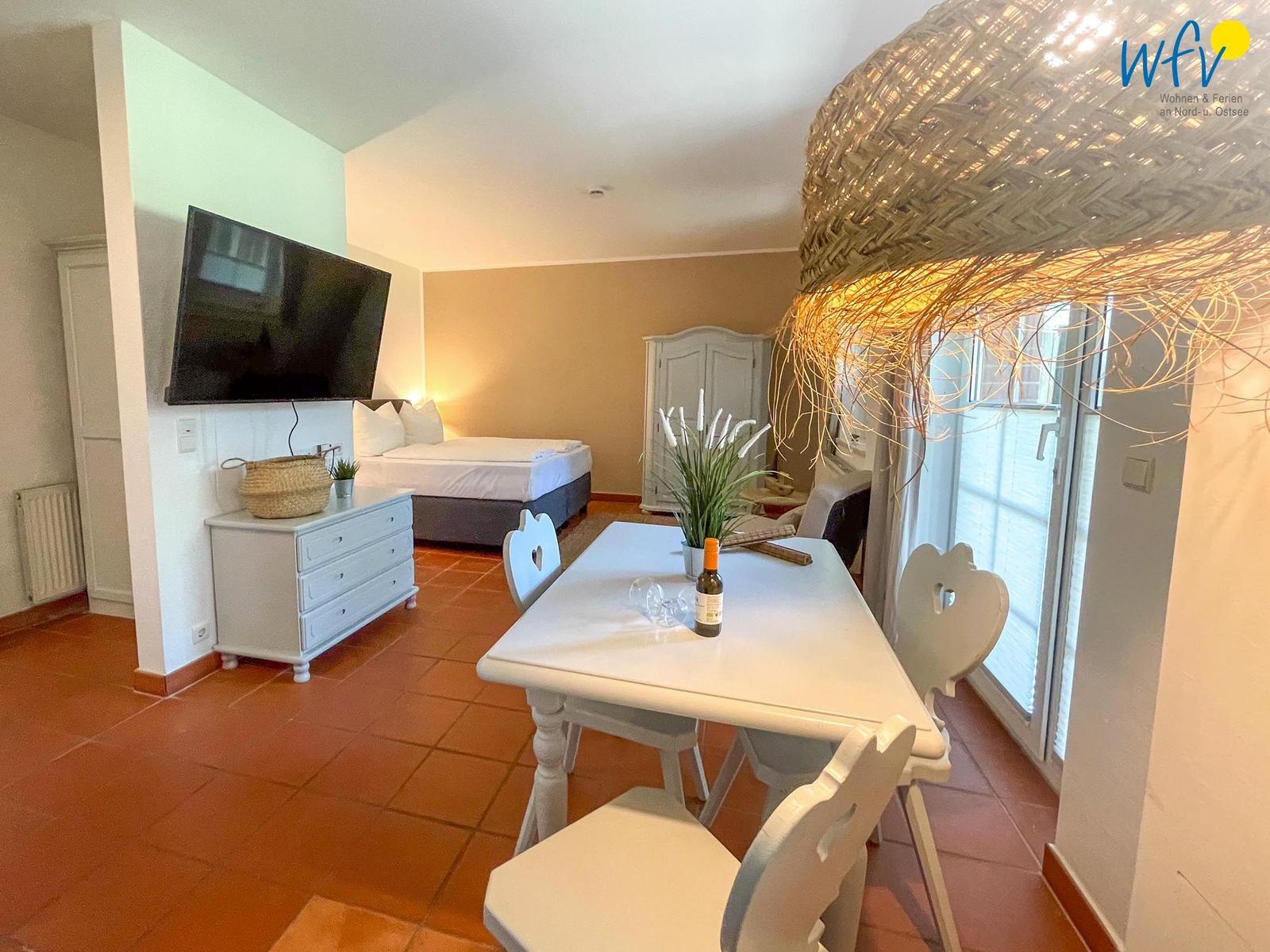 Wohnraum mit Schlafzimmer, Esstisch und Fernseher. Terrassentür und große Deckenleuchte.