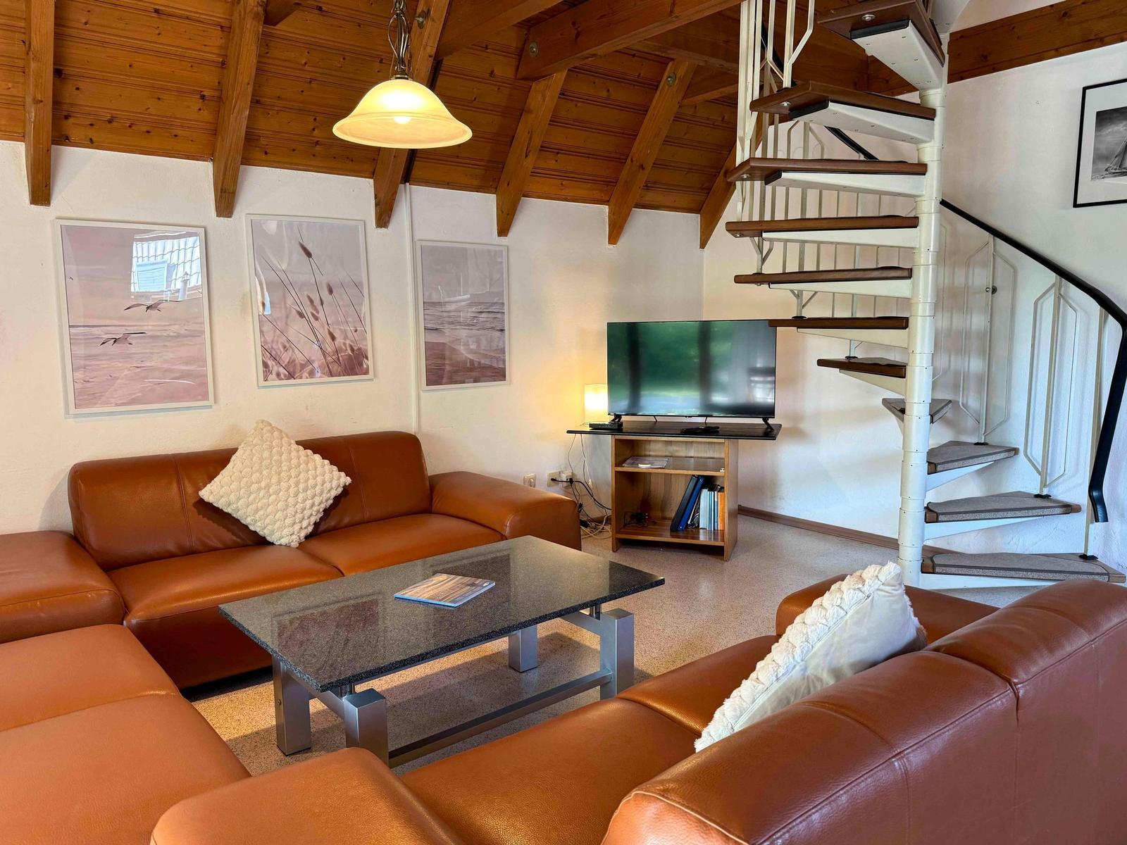 Wohnzimmer mit braunem Ledersofa, Glas-Tisch und Schraubenleiter.