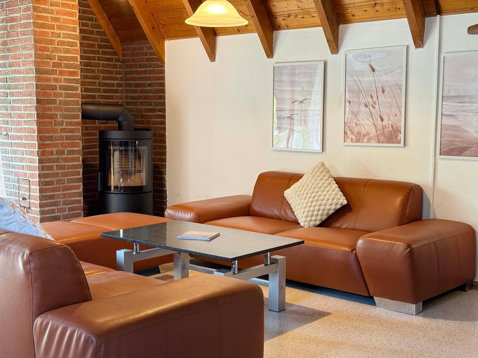 Ein Wohnzimmer mit braunem Ledersofa, Kaminofen und Holzbalkendecke.