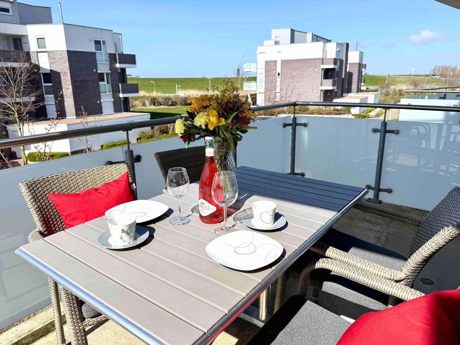 Terrasse mit Tisch, Stühlen und Blumen. Blick auf moderne Gebäude und Grünflächen.