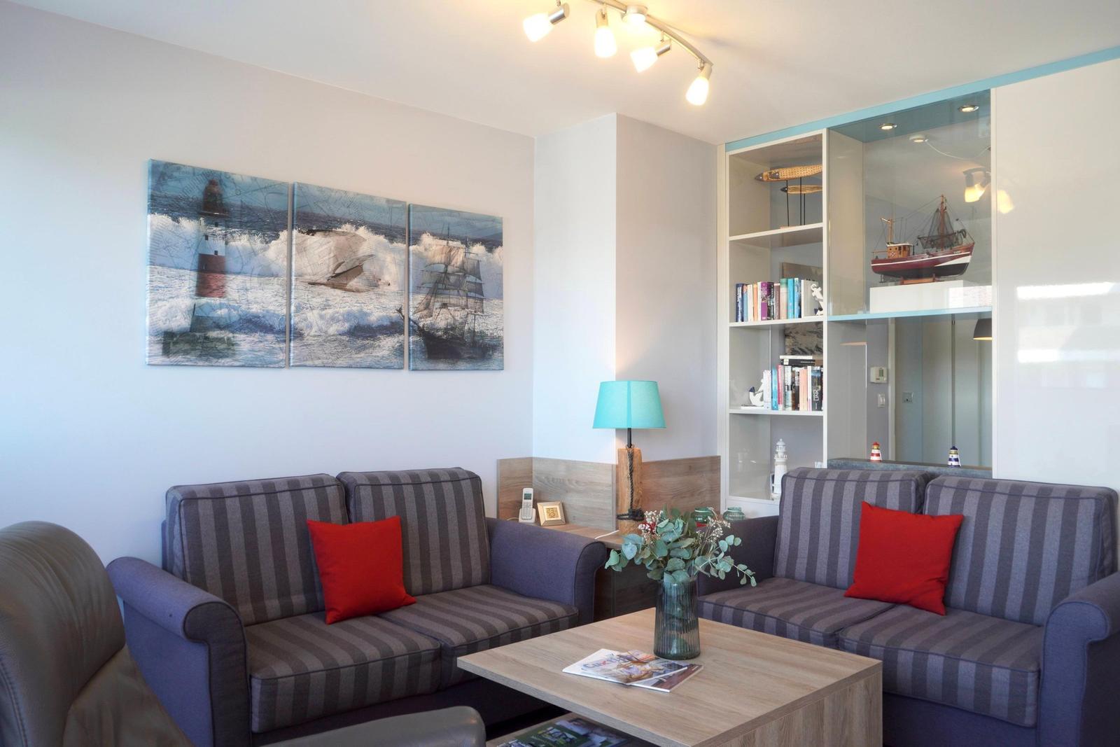 Wohnzimmer mit zwei Sofa, Tisch und Wandbildern mit Schiffen und Leuchtturm.