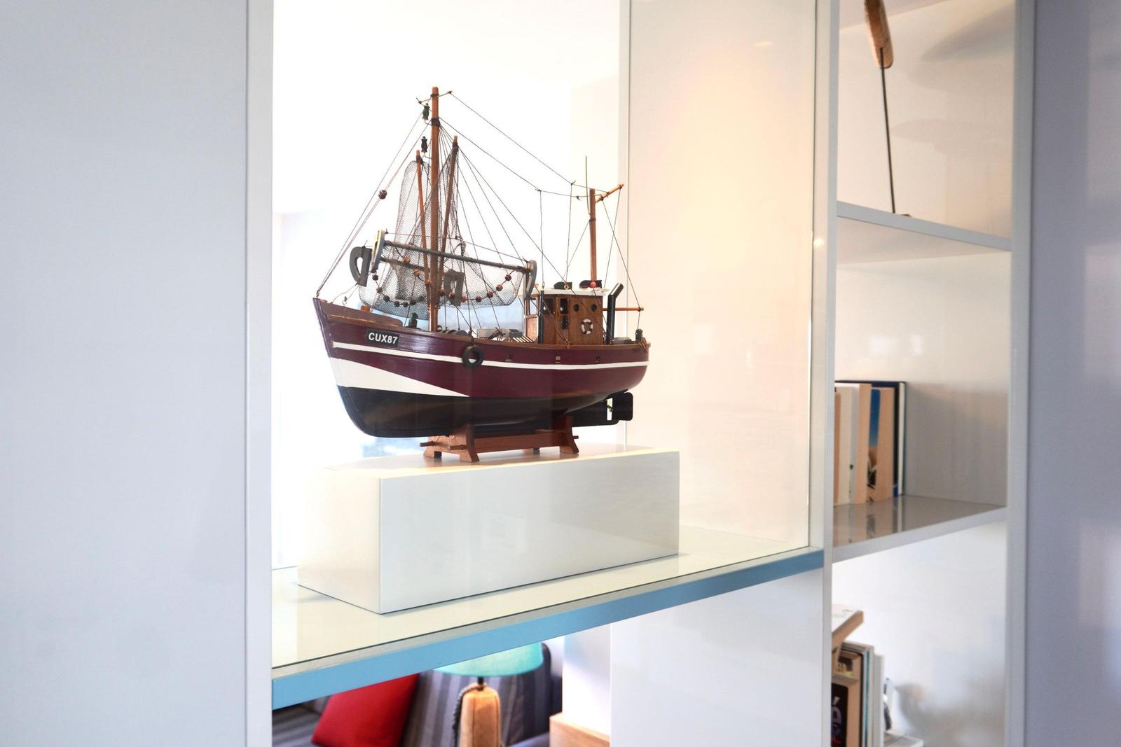 Ein hölzernes Schiffmodell mit dem Namen CUX87 steht auf einem weißen Sockel in einer Glasvitrine.