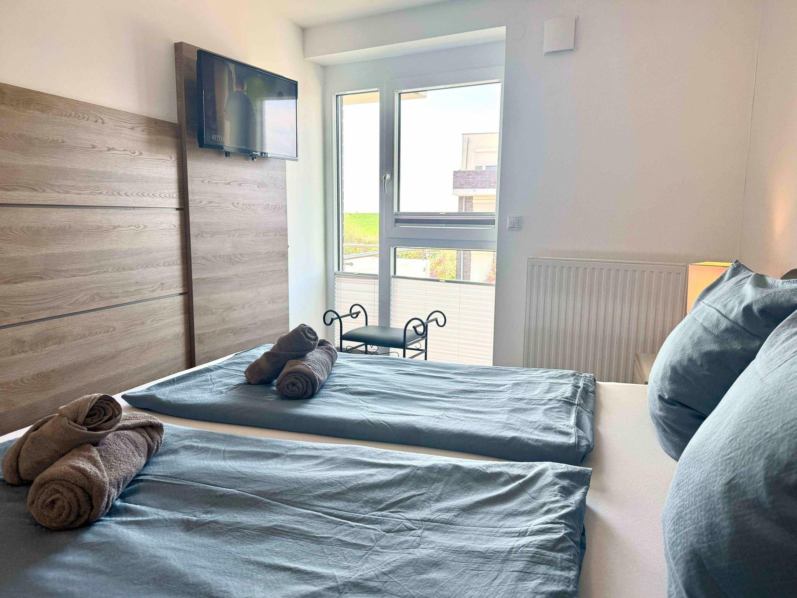 Schlafzimmer mit Doppelbett, TV und Balkon. Handtuchrollen auf dem Bett.