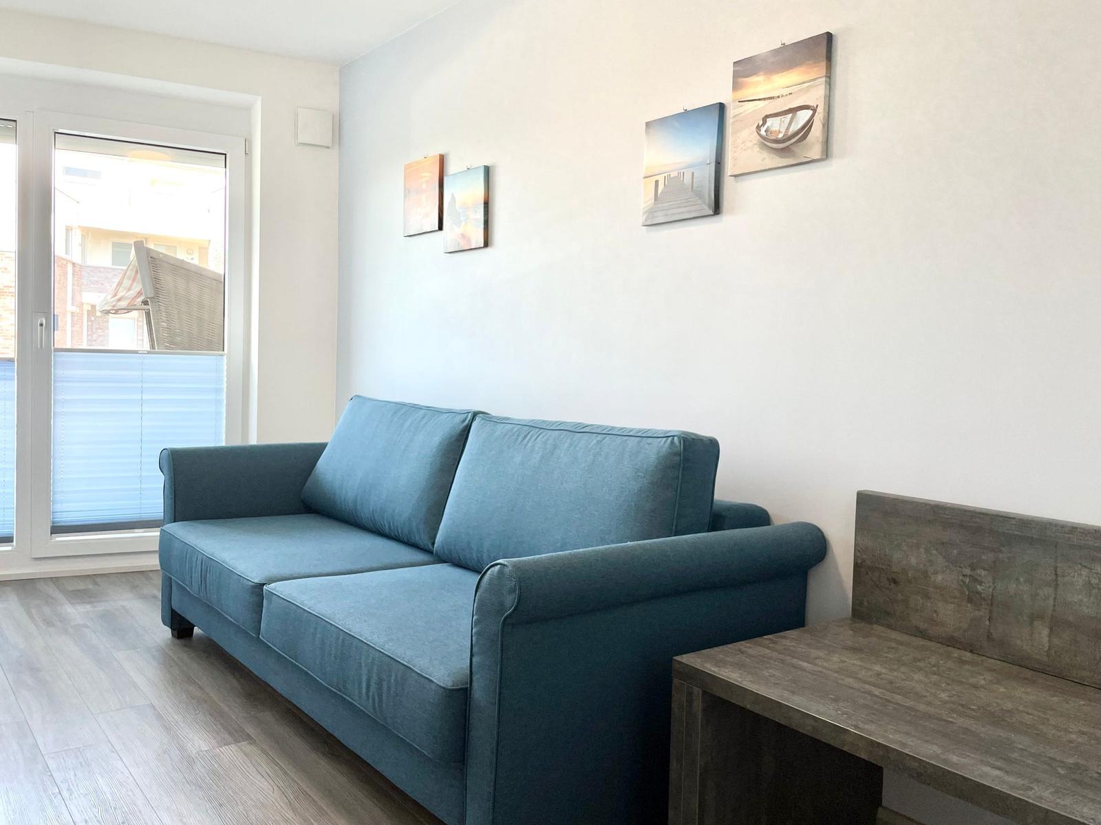 Ein Wohnzimmer mit blauem Sofa, Holzboden und Wandbildern an der Wand.