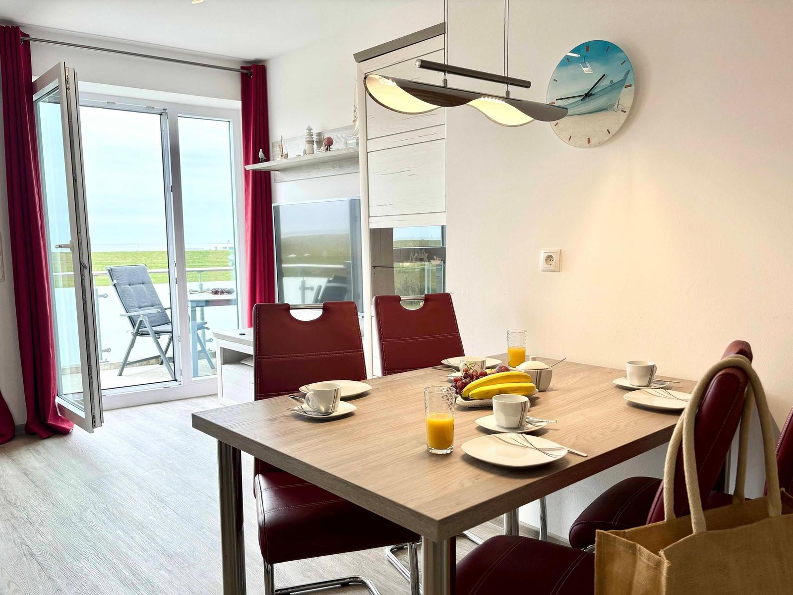 Dining room with table, chairs, and view to balcony. Wall clock and lamp visible.