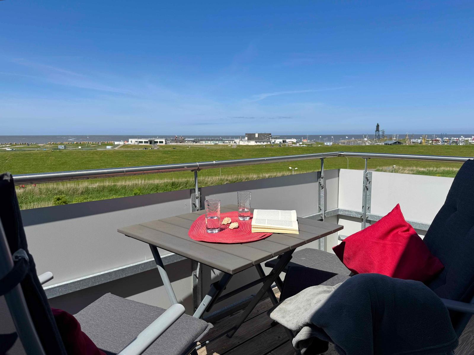 Terrace with table, chairs, and view of grassland and sea.