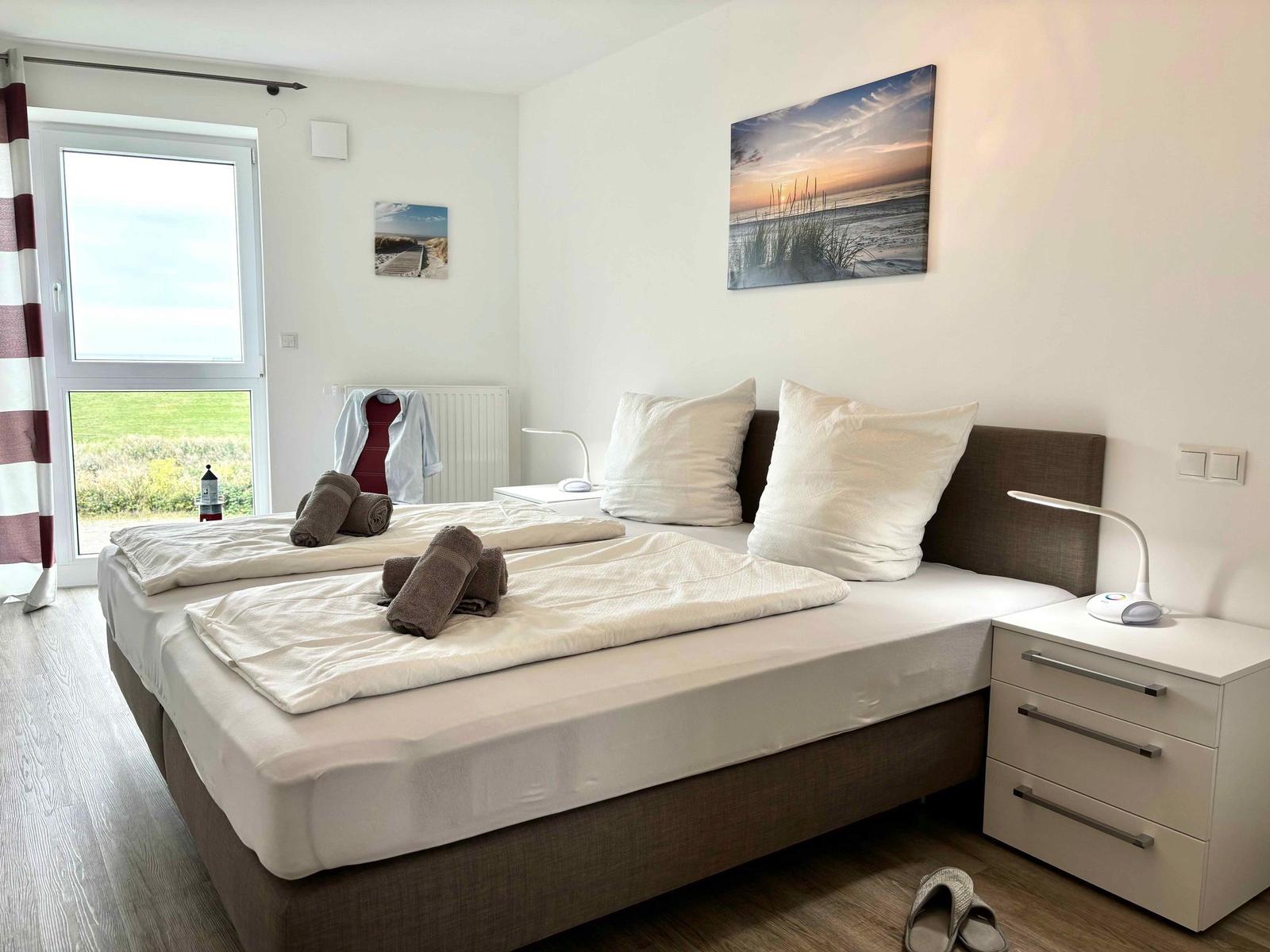 Bedroom with double bed, nightstand, and window view of green field.