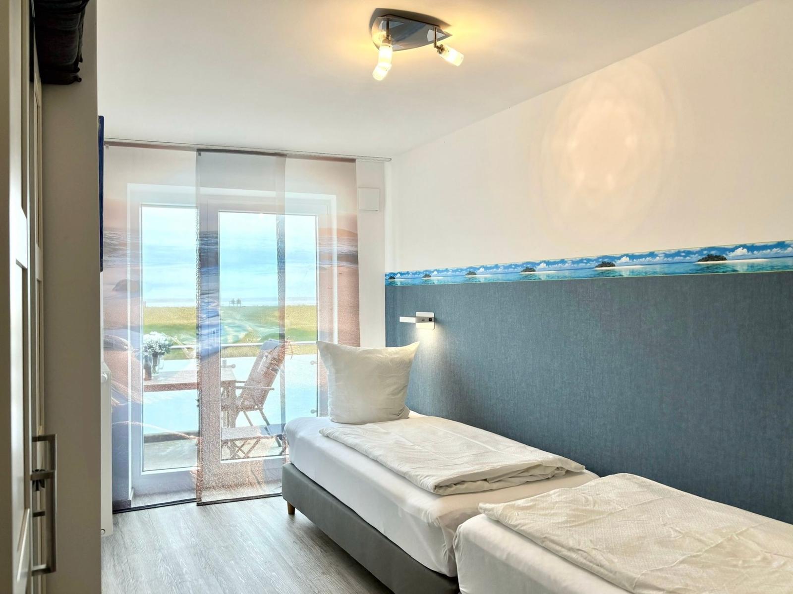 Room with view of balcony and beach. Bed with white bedding and wall with beach motif.