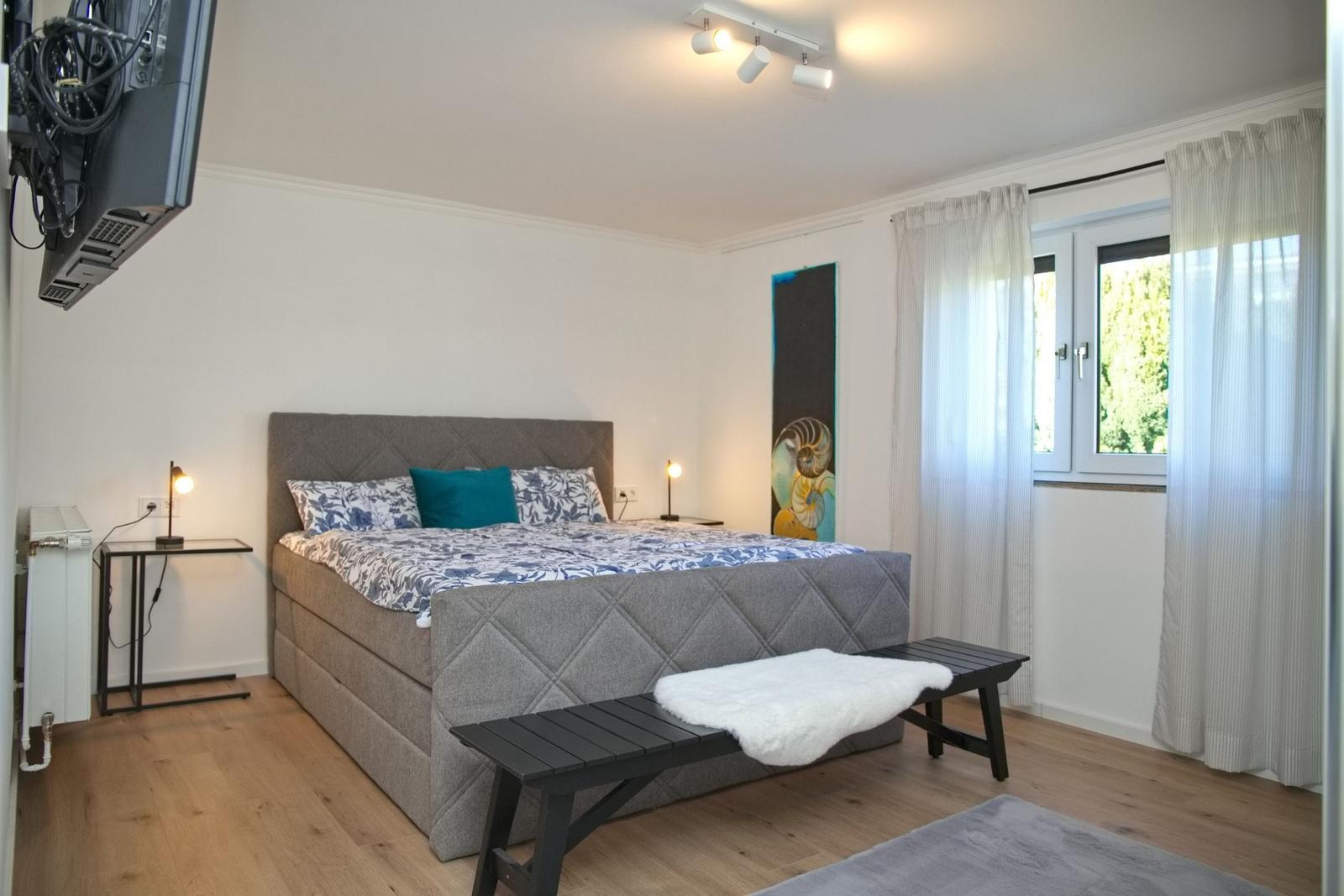Schlafzimmer mit Bett, Fenster, Nachttisch und Wandbild.