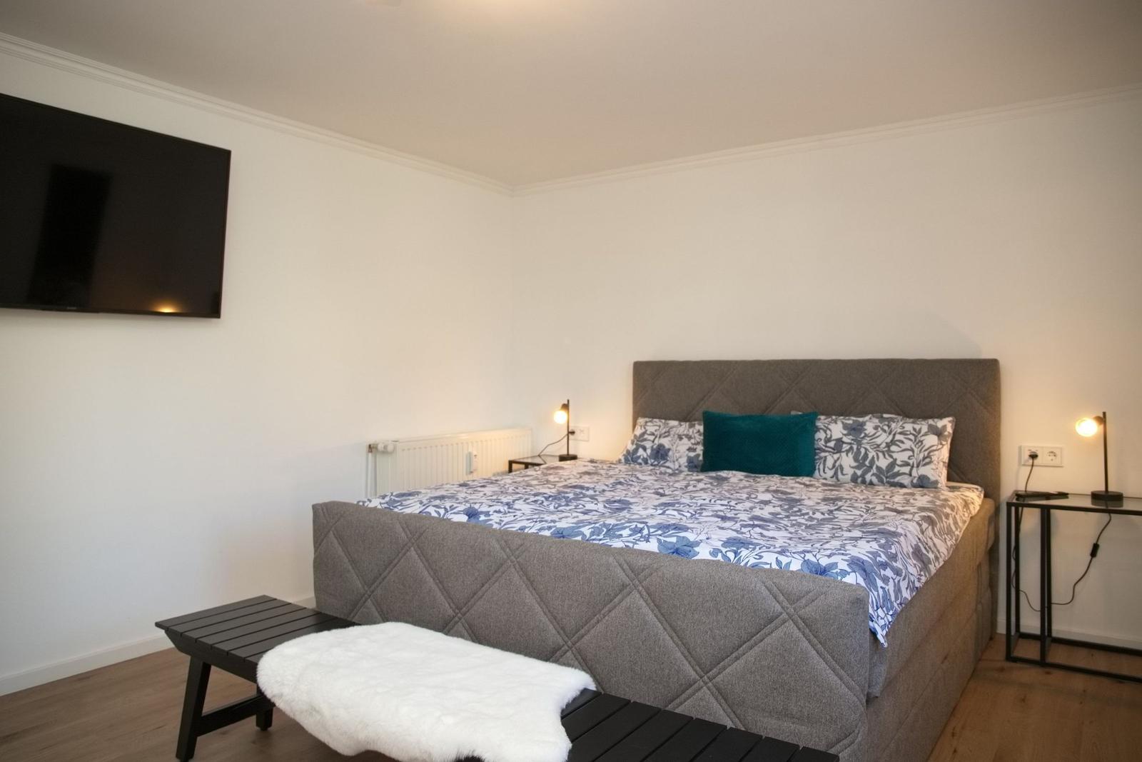 Schlafzimmer mit Bett, Fernseher und Nachttischen.