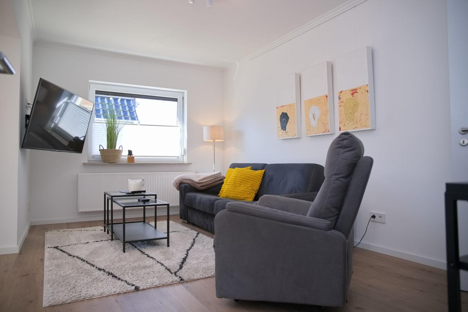 Wohnzimmer mit Sofa, Sessel, Fernseher und Fenster