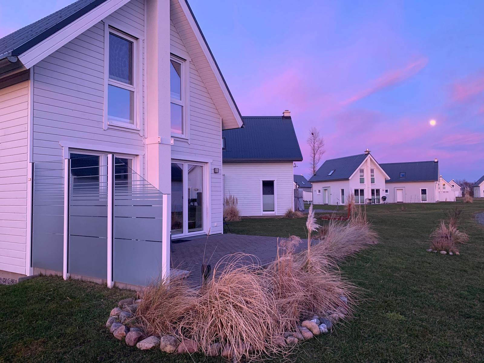 Moderne Häuser mit Holzfassade und dunklem Dach, umgeben von Gras und Steinen bei Dämmerung.