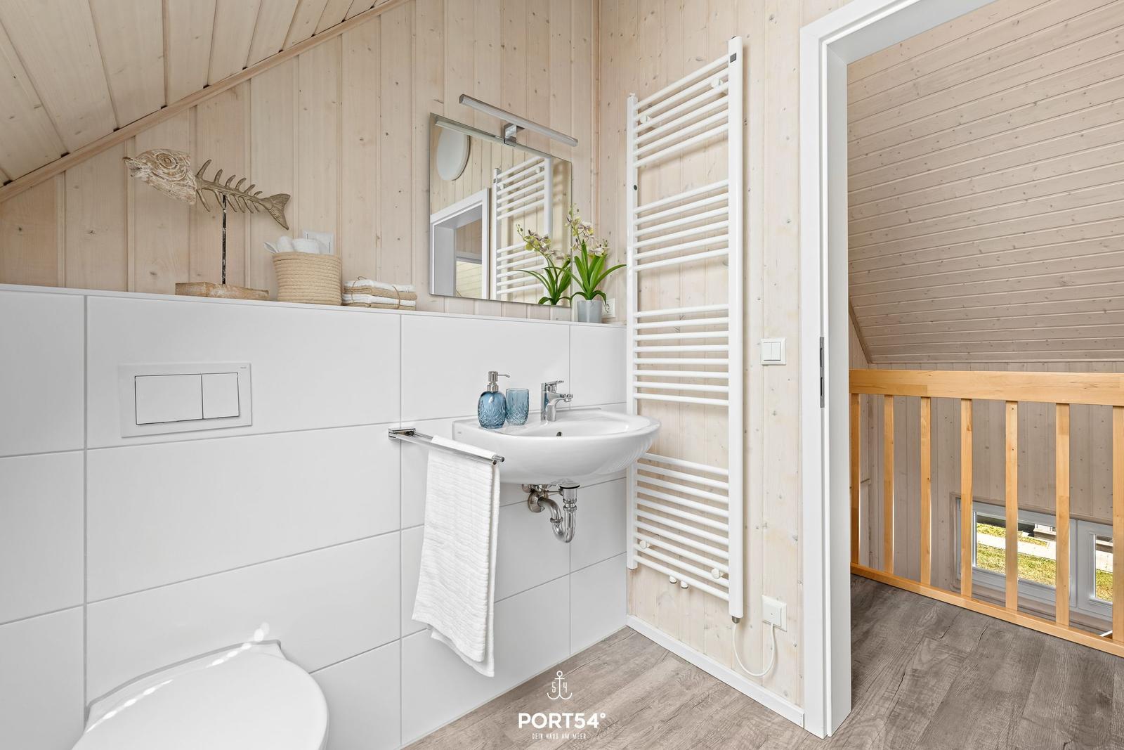Badezimmer mit Waschbecken, Spiegel und Heizkörper. Holzwände und Fliesen.