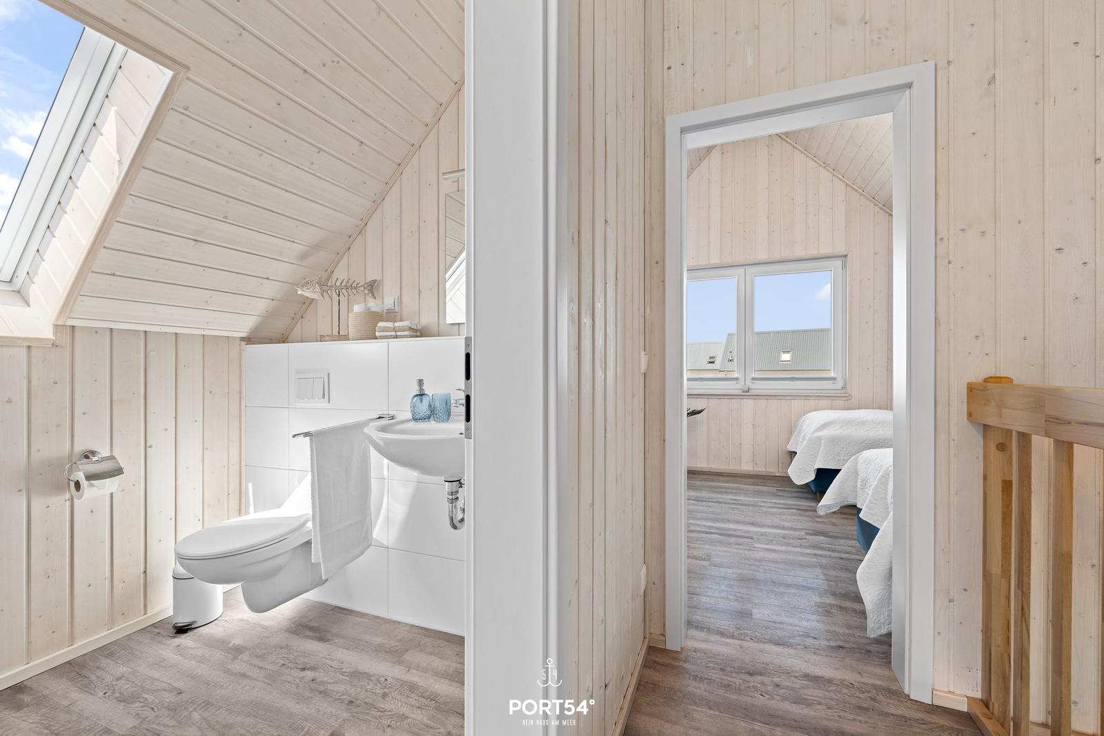 Badezimmer mit Toilette und Waschbecken. Durchgang in Schlafzimmer mit zwei Betten.