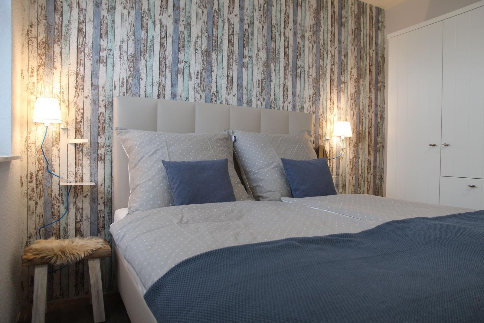 Schlafzimmer mit Bett, Kopfteil, Kissen, Wandtapete und Kleiderschrank.