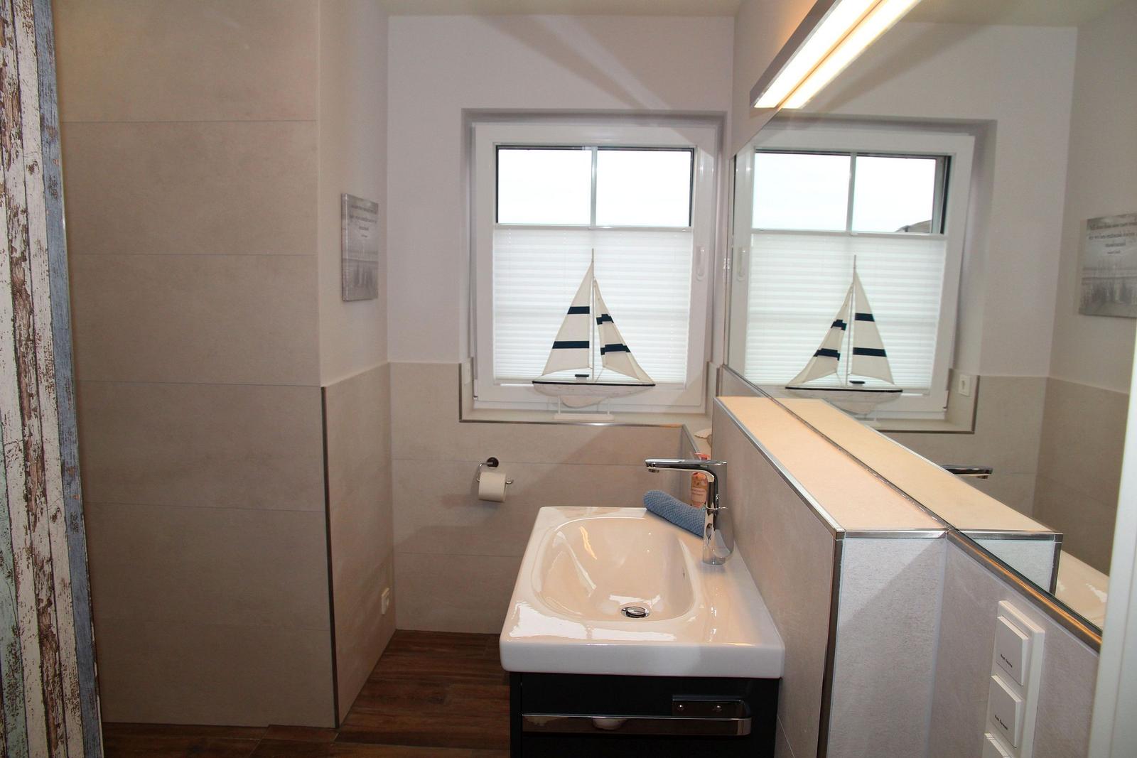 Badezimmer mit Waschbecken, Spiegel und Segelboot auf dem Fensterbrett.