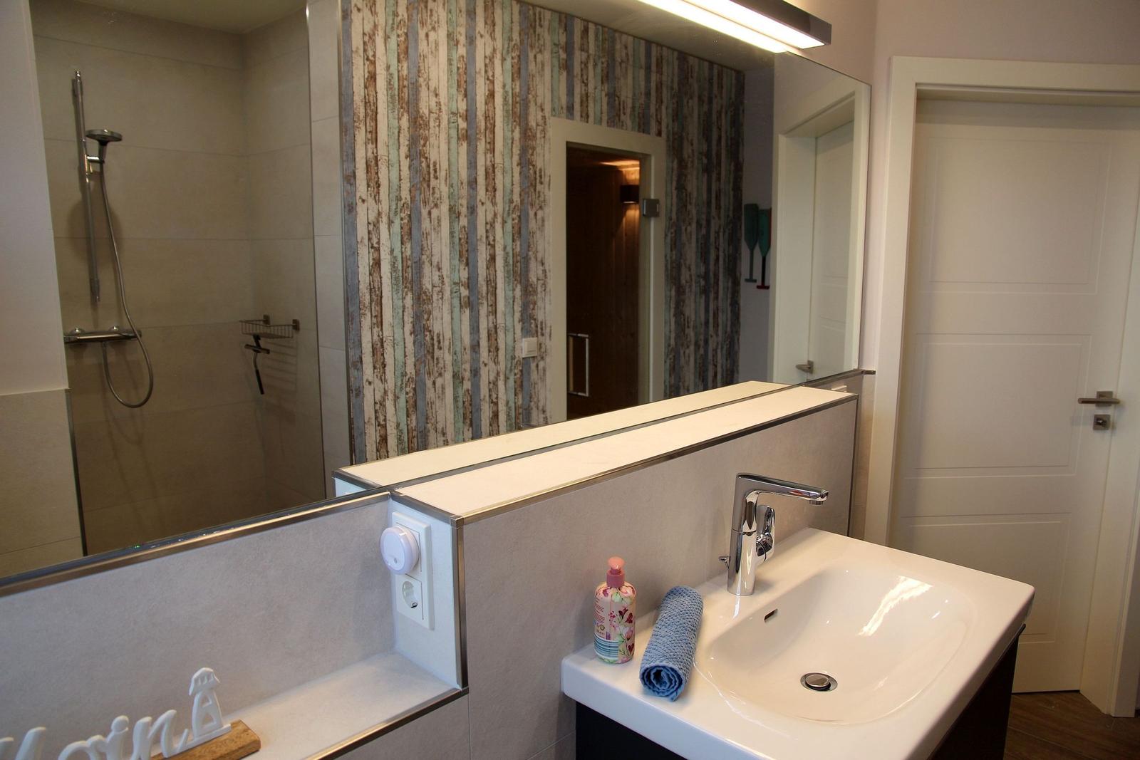 Badezimmer mit Dusche, Waschbecken und Spiegel. Wand mit Streifenmuster.