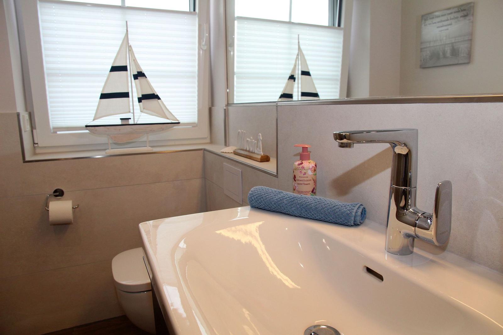 Badezimmer mit Waschbecken, Spiegel und Segelboot-Dekoration am Fenster.