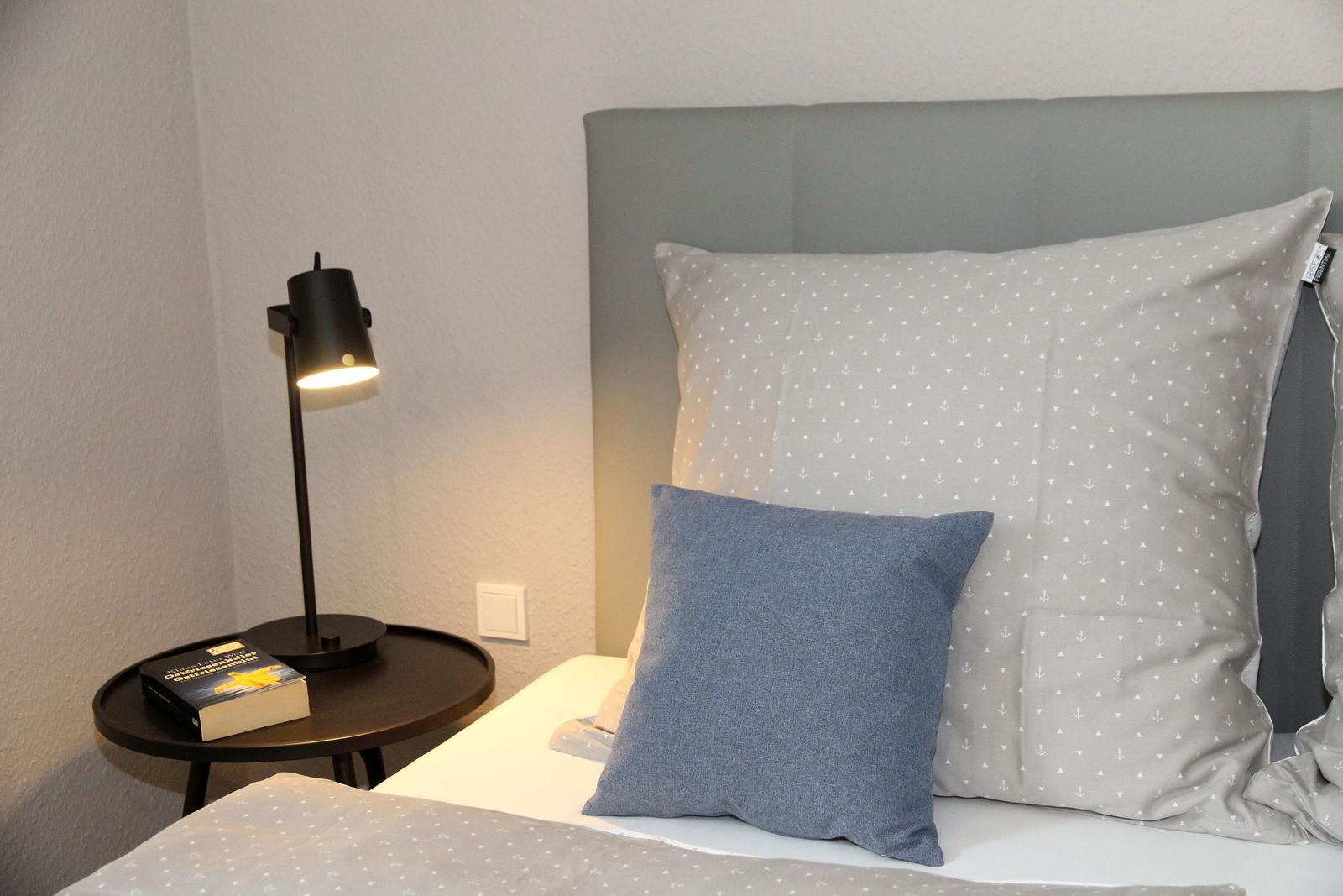 Schlafzimmer mit Bett, Kissen und Nachttisch mit Lampe und Buch.