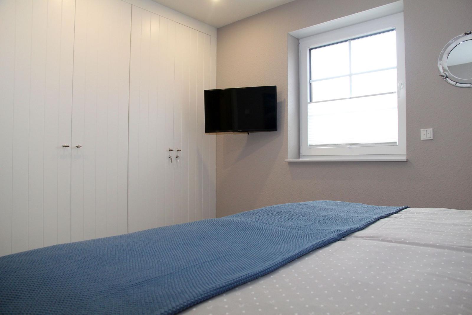 Schlafzimmer mit Bett, Fenster, TV und Schrank.