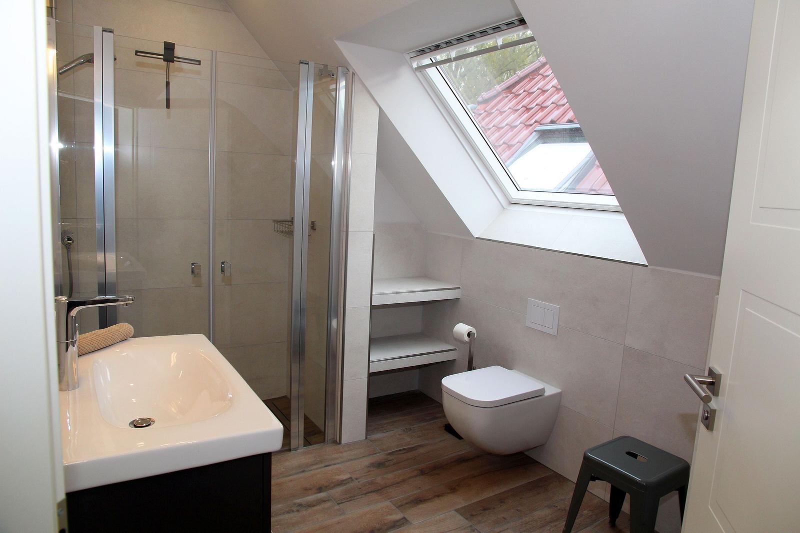 Badezimmer mit Dusche, Waschbecken und Toilette unter Dachfenster.
