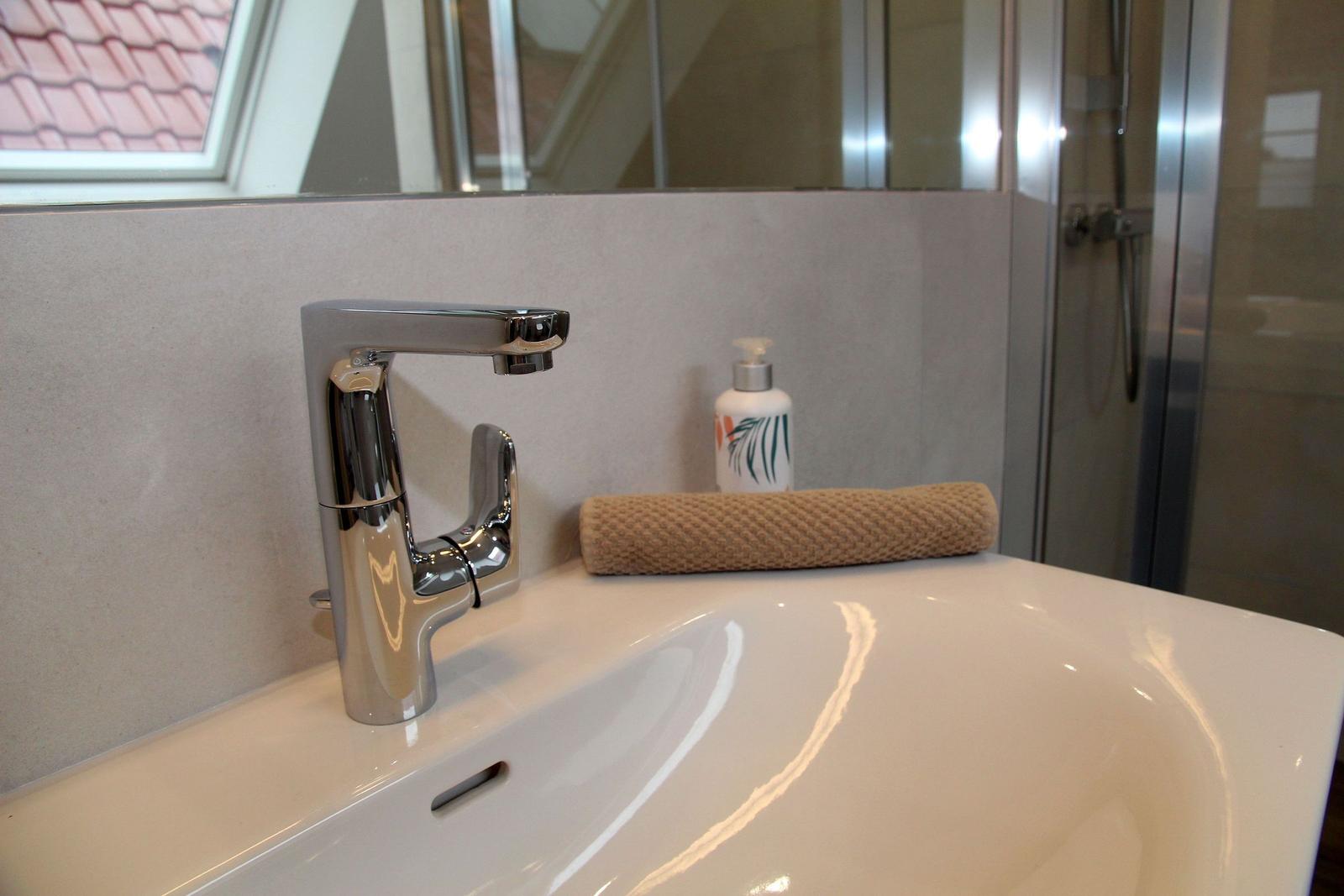Waschbecken mit Wasserhahn, Handtuch und Seife. Dusche und Fenster sind sichtbar.