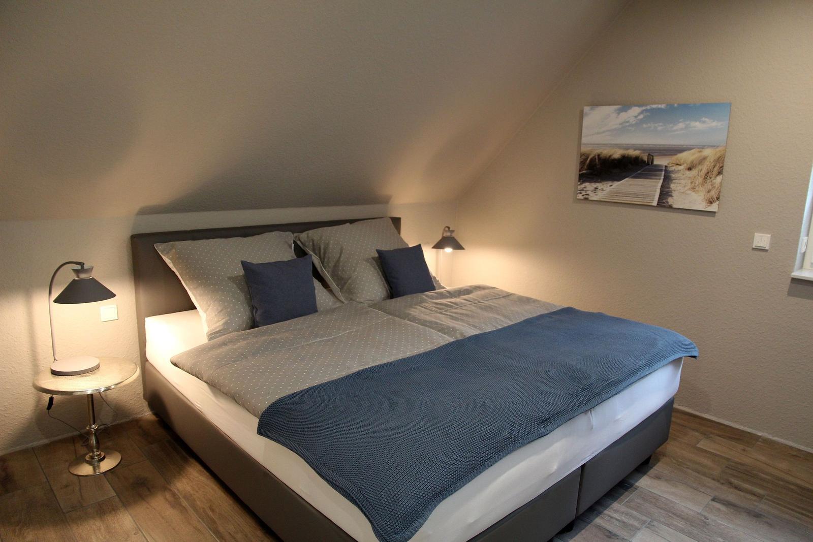 Schlafzimmer mit Doppelbett, Nachttisch und Wandbild. Holzboden und schräges Dach.