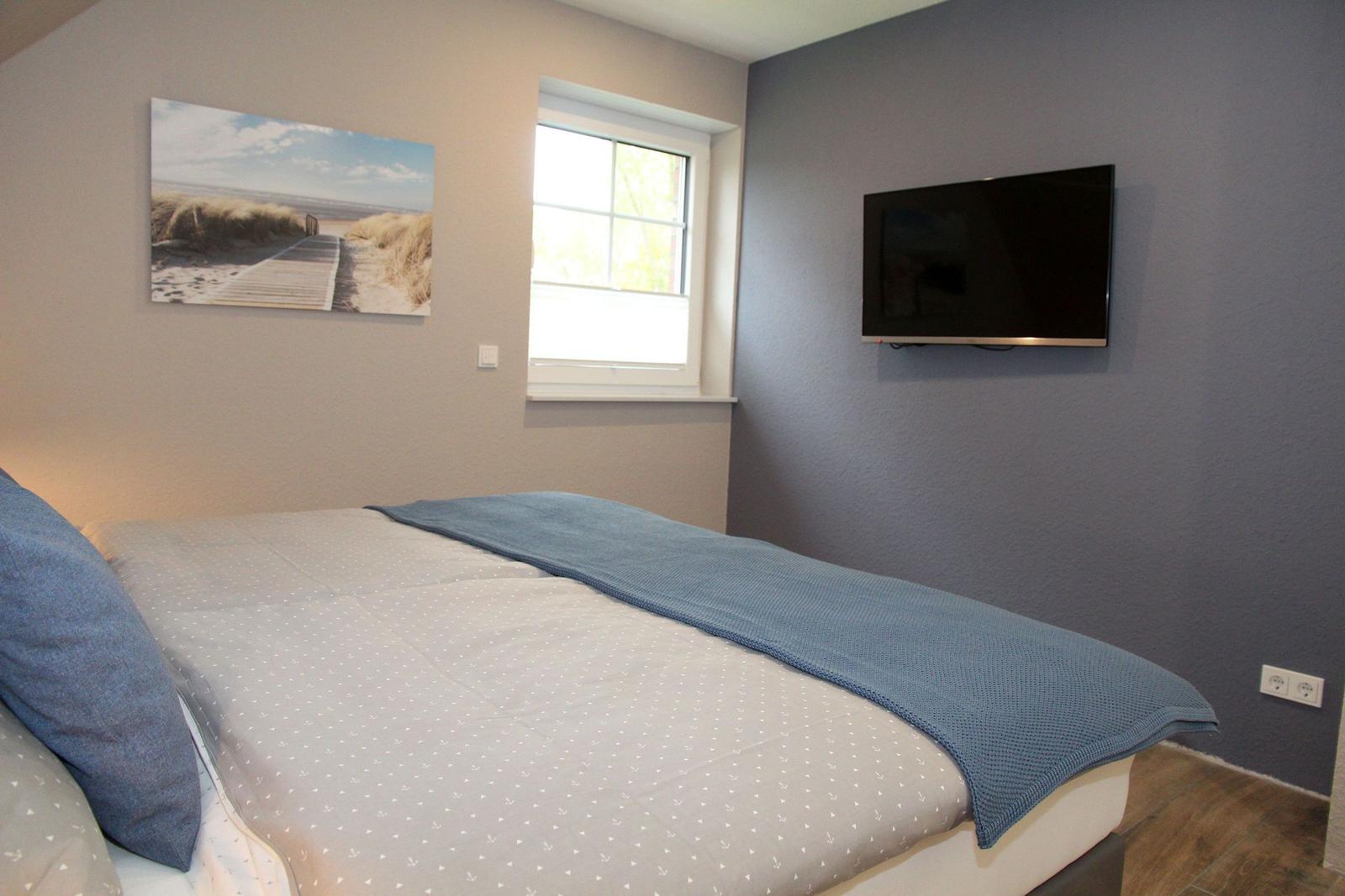 Schlafzimmer mit Bett, Wandbild, Fenster und Wand-TV.