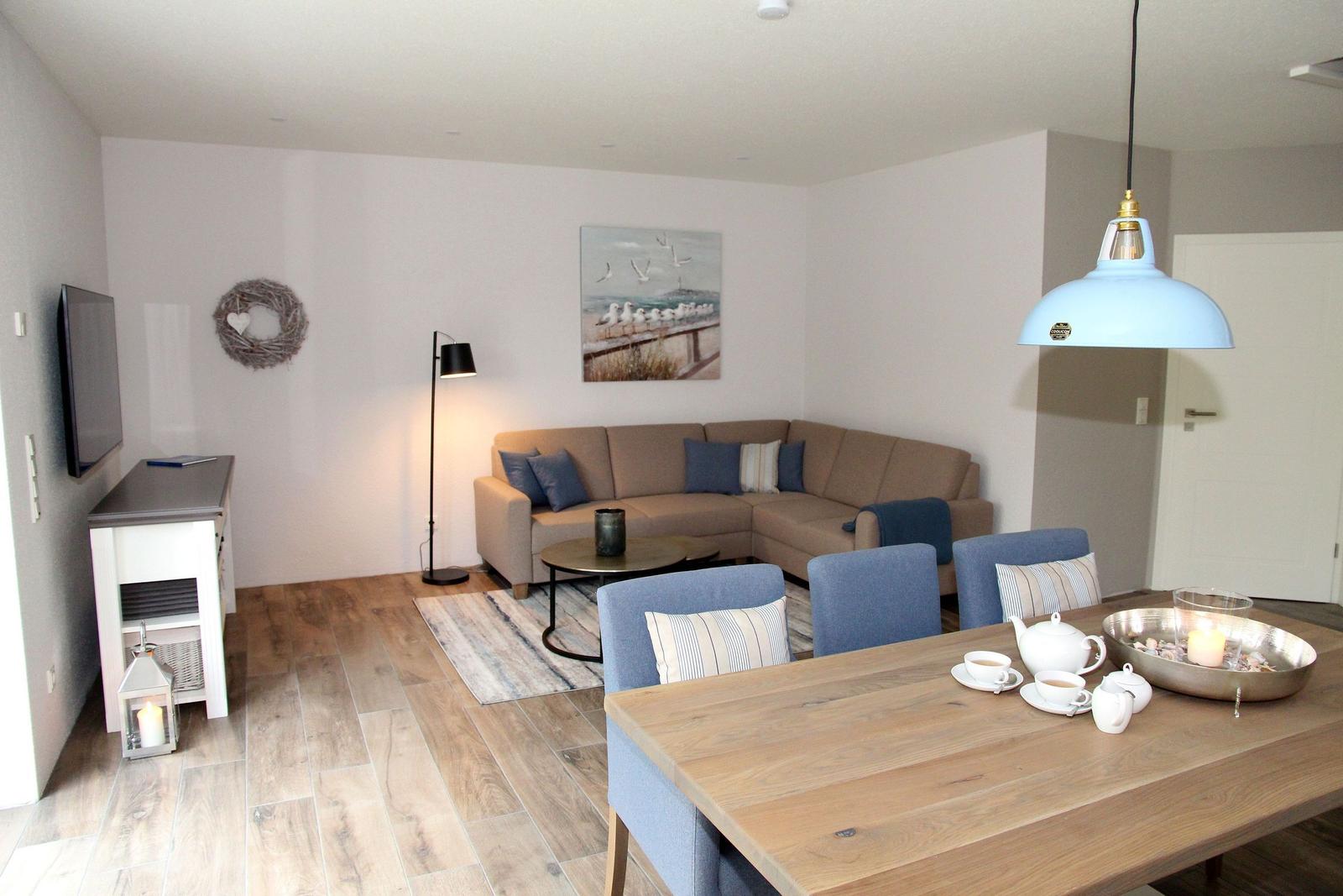 Wohn- und Essbereich mit Sofa, Tisch und Stühlen. Wandbild und Deckenleuchte sichtbar.