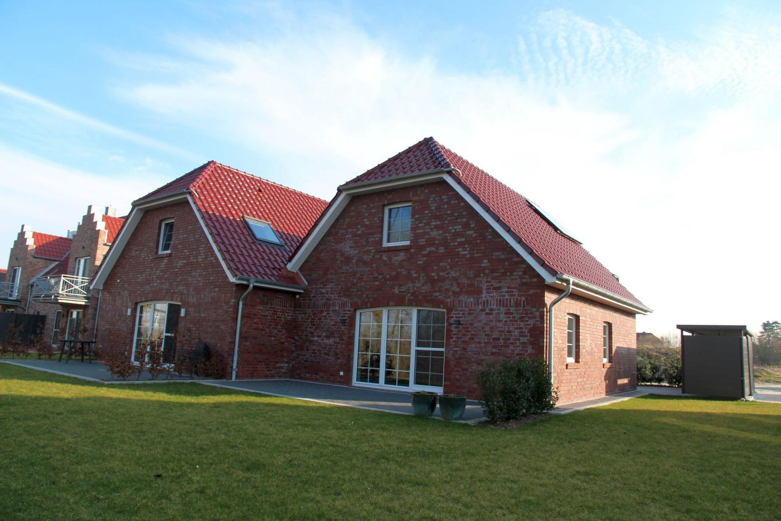 Rotes Ziegelhaus mit Dachgauben und großem Garten. Terrasse mit Tisch und Stühlen.