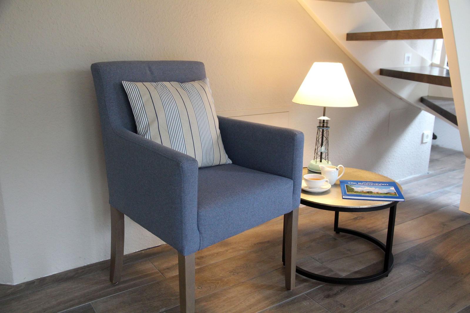 Ein blauer Sessel mit Kissen steht neben einem runden Tisch mit Lampe und Tasse.
