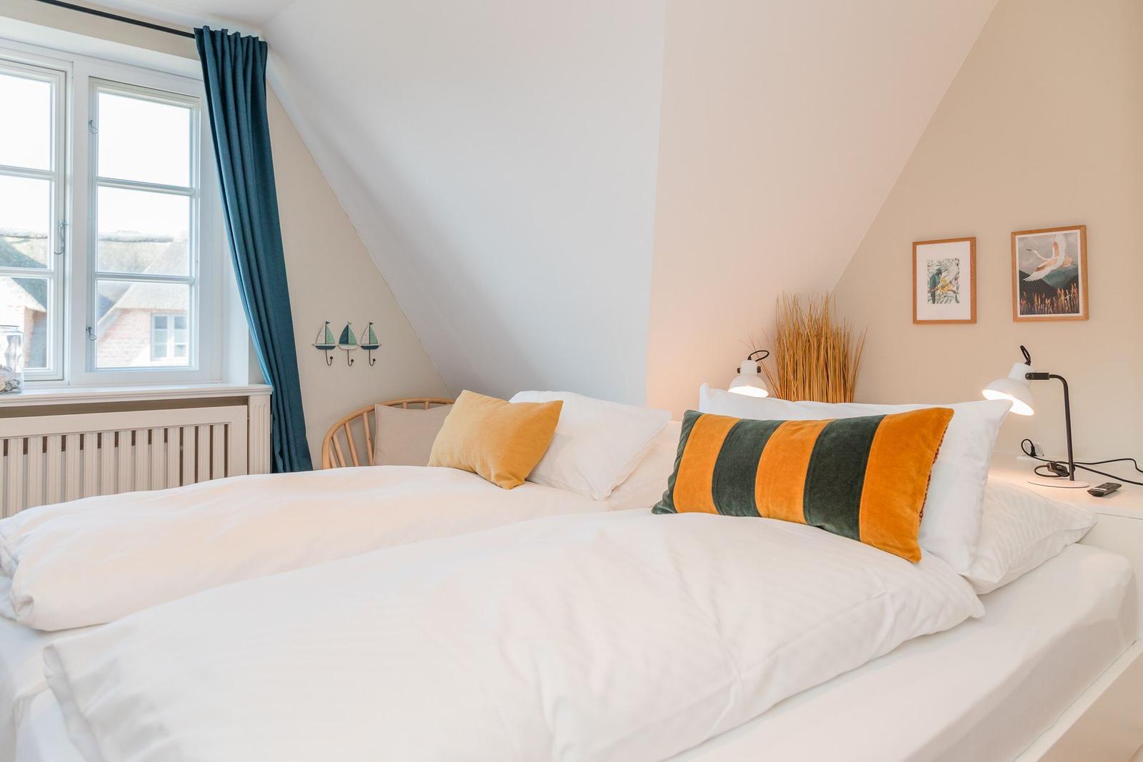 Ein Schlafzimmer mit Dachschrägen, weißem Bett und blauen Vorhängen.