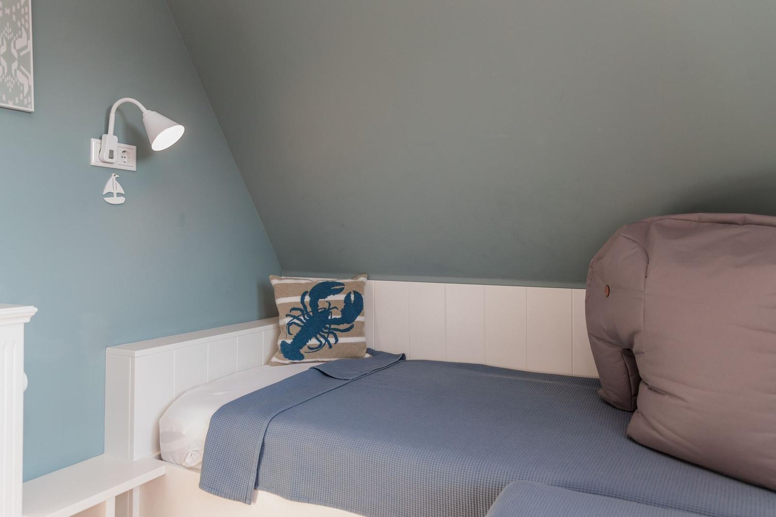 Schlafzimmer mit Bett, Kissen und Wandlampe unter schräger Decke.