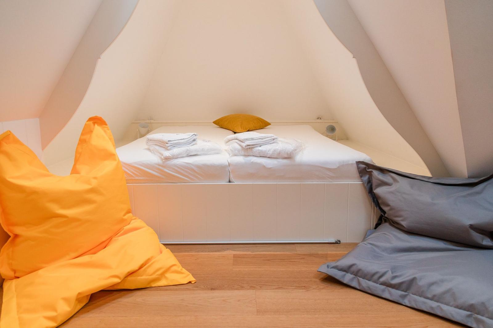 Schlafzimmer mit Doppelbett, gelben und grauen Kissen und Holzboden.