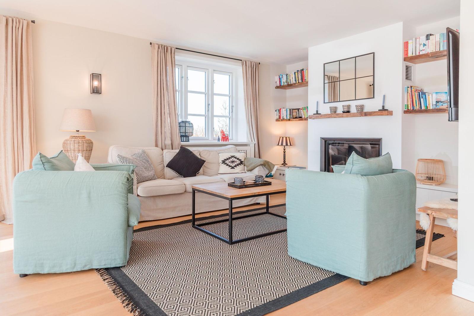 Wohnzimmer mit Sofa, zwei Sesseln, Kamin und Bücherregalen.