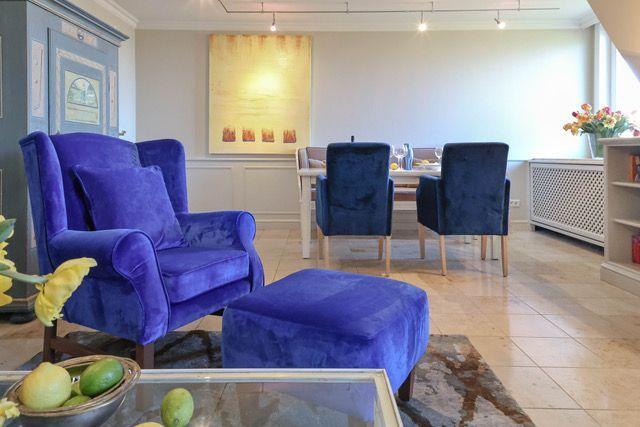 Lounge mit blauer Sitzgarnitur und Esstisch mit Stühlen im Hintergrund.