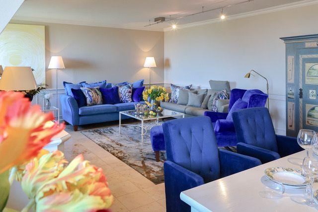 Wohnzimmer mit blauen Sofas, Glas-Tisch und dekorativen Kissen.