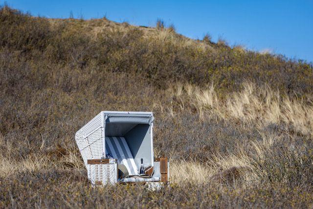 Weißer Strandkorb auf Dünen mit Getränk und Sonnenschirm