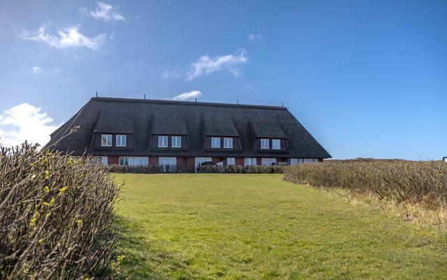 Haus mit strohgedecktem Dach und großem Garten unter blauem Himmel.