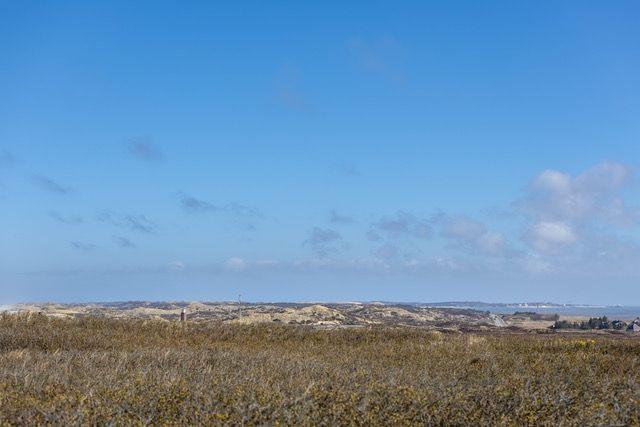 Weitläufiger Blick auf eine hügelige Landschaft unter blauem Himmel mit vereinzelten Wolken.