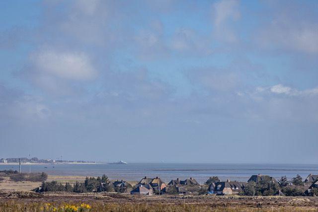 Meer mit Häusern im Vordergrund und einem Schiff im Hintergrund unter blauem Himmel.