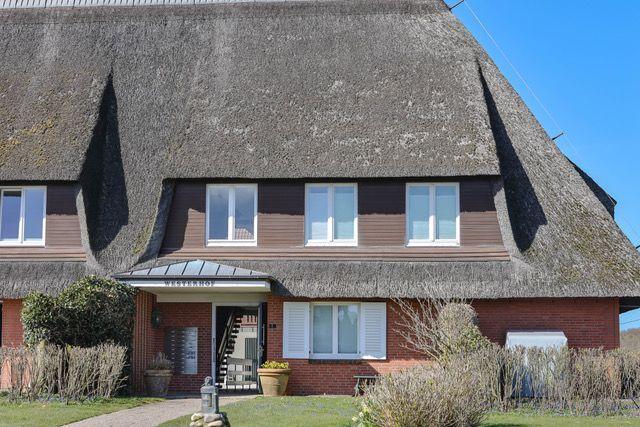 Haus mit Strohdach, Eingangstür und Fenstern. Vorgarten mit Pflanzen und Steinen.