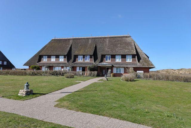 Haus mit Strohdach, Rasenfläche und Steintreppe zum Eingang.