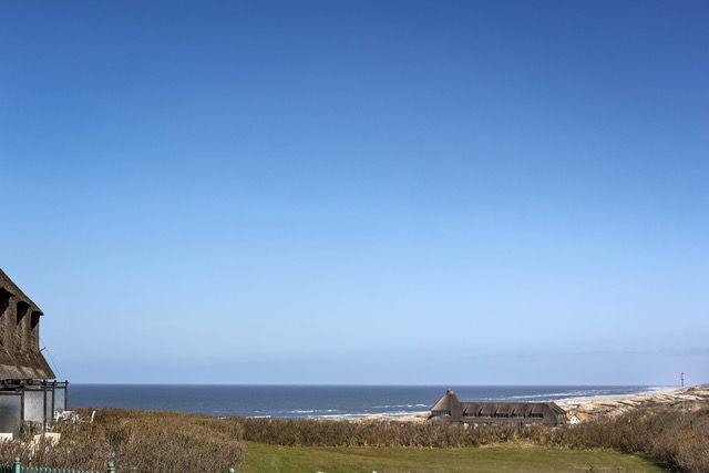 Meer und Strand mit Dächern im Vordergrund unter blauem Himmel.