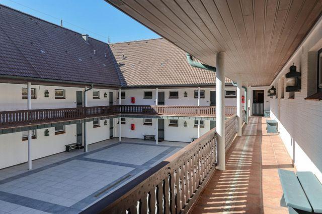 Hof mit Terrasse, Holzgeländer und mehreren Gebäuden mit Fenstern.